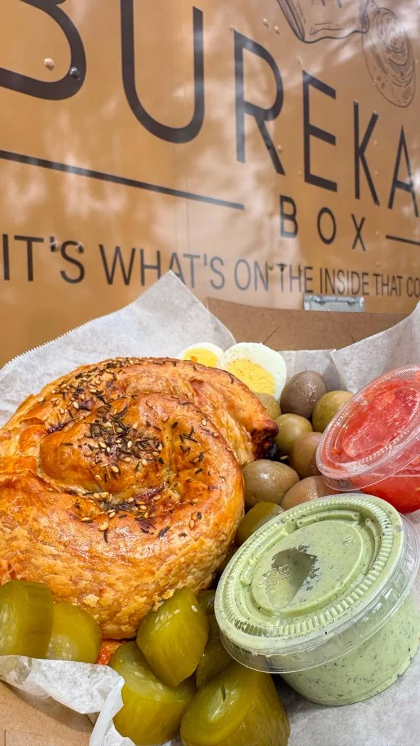 Round pizza burekas with egg, olives and dips in Burekas Box packaging