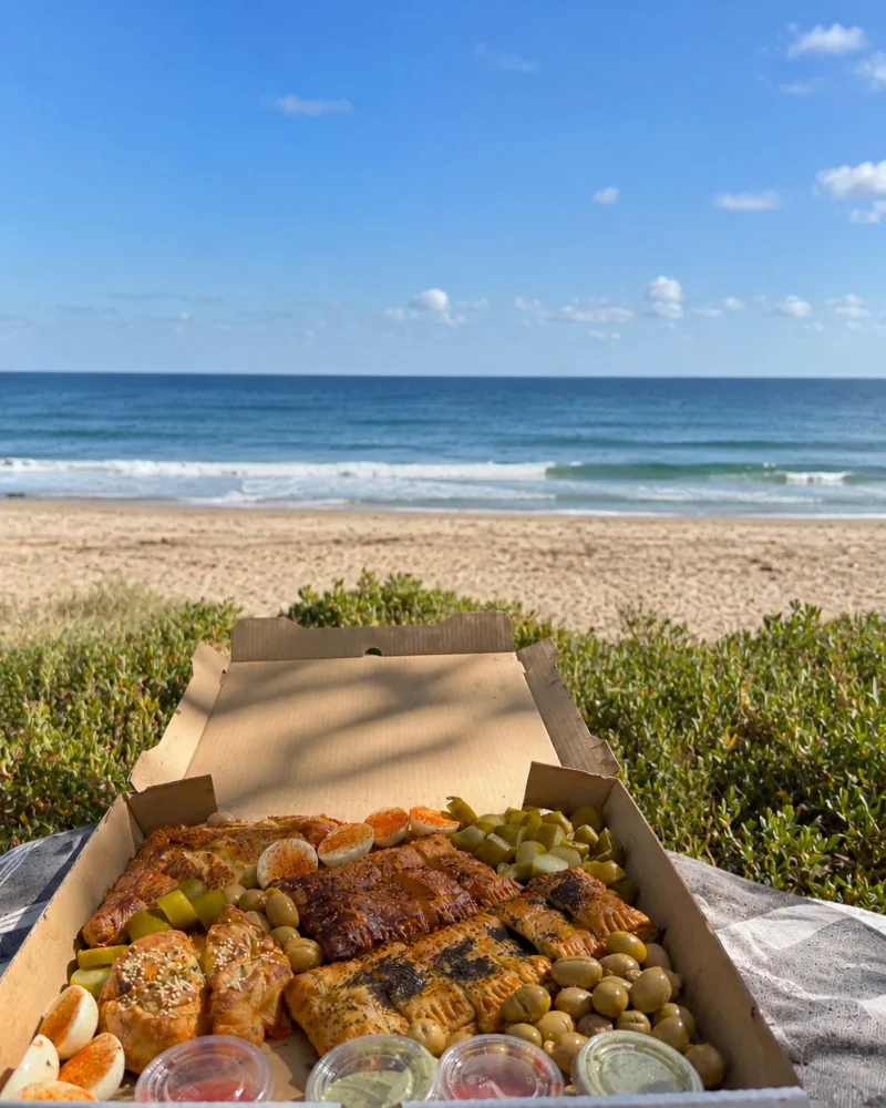 An open box of burekas and sides by the beach