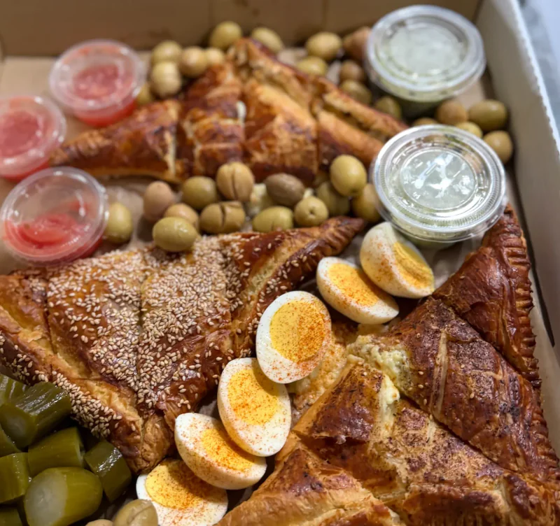 A Burekas Box spread with savory pastries, eggs, olives, pickles and dips